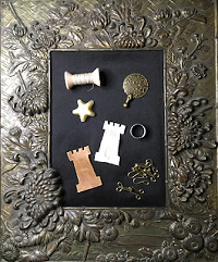 Contents of a small period sewing kit (felt tower with 3 fine steel needles, linen thread on a wood spool, leather thread puller, thimble, beeswax, 4 pairs of hooks and eyes, and a thread cutter) photographed in an ornate frame